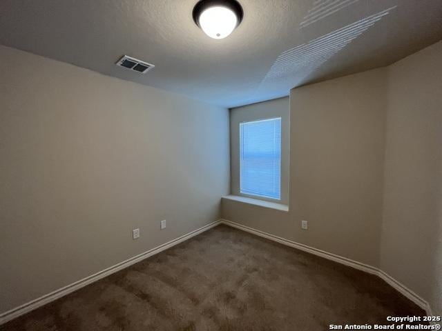 empty room featuring a textured ceiling, dark carpet, visible vents, and baseboards