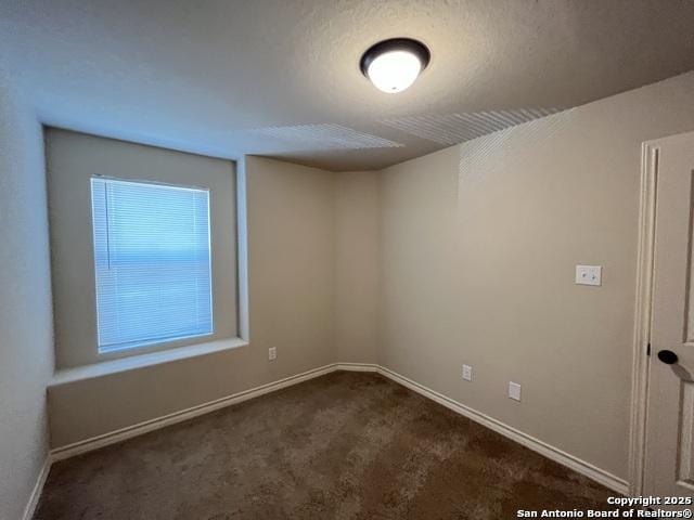 empty room with dark colored carpet, a textured ceiling, and baseboards