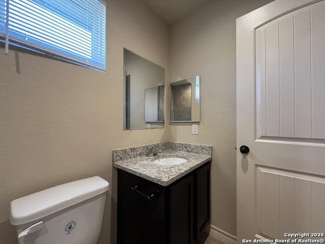 half bathroom featuring a textured wall, vanity, and toilet