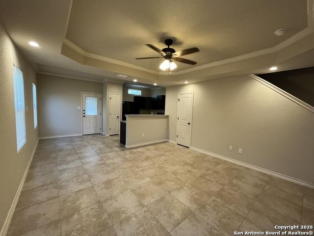 unfurnished living room with a raised ceiling, crown molding, and baseboards