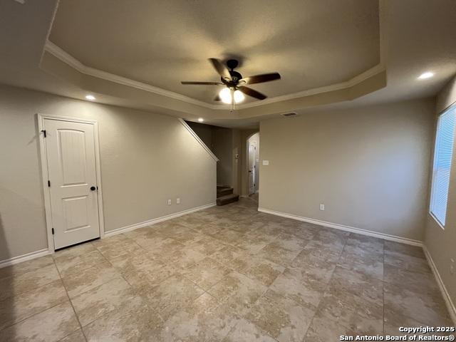 unfurnished room with a ceiling fan, baseboards, stairs, ornamental molding, and a tray ceiling