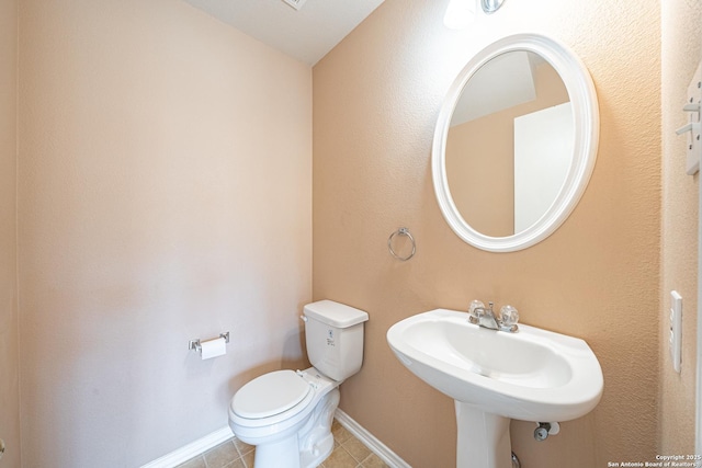 half bath featuring tile patterned flooring, baseboards, a sink, and toilet