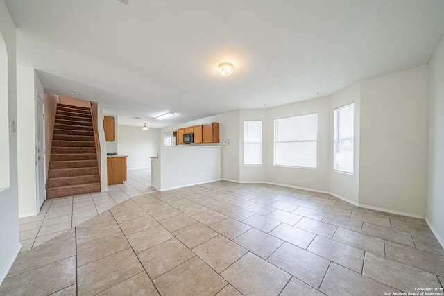 unfurnished living room with stairs, light tile patterned floors, and baseboards