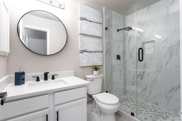 bathroom with toilet, a textured wall, a marble finish shower, and vanity