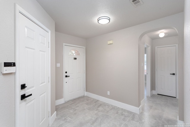 foyer entrance with arched walkways, visible vents, a textured ceiling, and baseboards