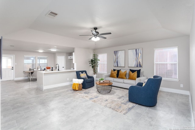 living area with a tray ceiling, visible vents, ceiling fan, and baseboards