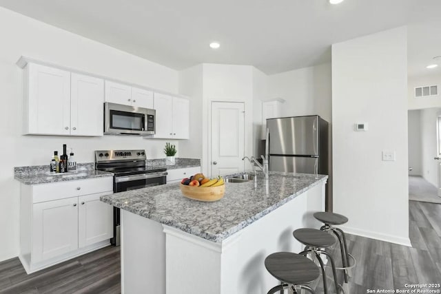 kitchen featuring visible vents, a kitchen island with sink, stainless steel appliances, white cabinetry, and a sink