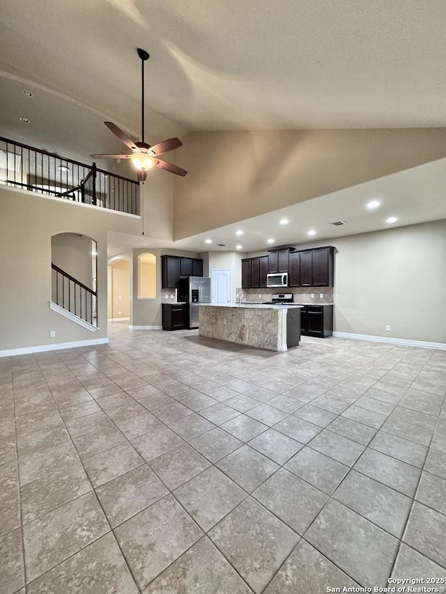 unfurnished living room featuring light tile patterned floors, baseboards, arched walkways, ceiling fan, and stairs