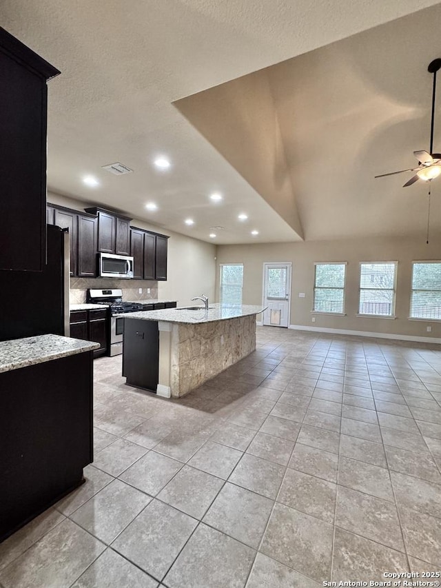 kitchen featuring light stone countertops, a kitchen island with sink, stainless steel appliances, and open floor plan