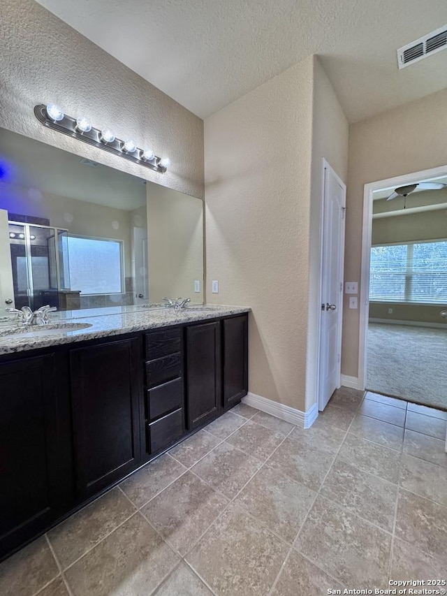 bathroom featuring a textured ceiling, a sink, visible vents, baseboards, and double vanity