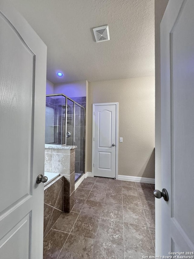 full bathroom featuring a textured ceiling, visible vents, baseboards, a shower stall, and a bath