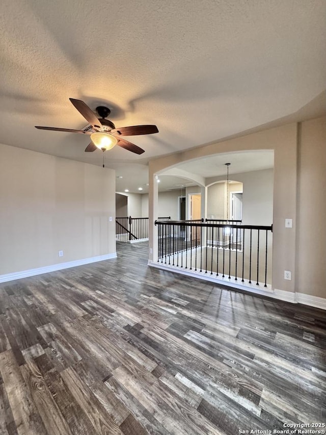 empty room with dark wood finished floors, a textured ceiling, and baseboards