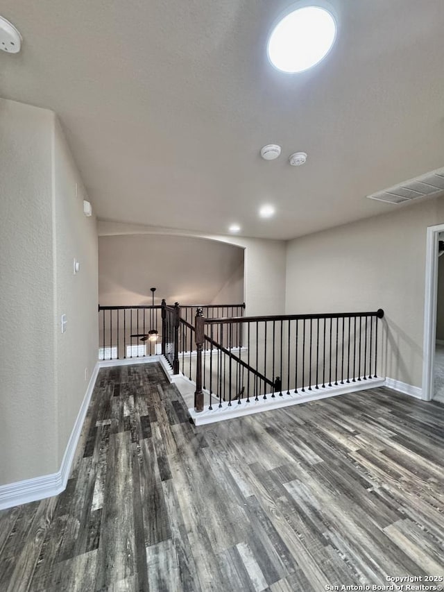 hallway featuring visible vents, baseboards, wood finished floors, and an upstairs landing