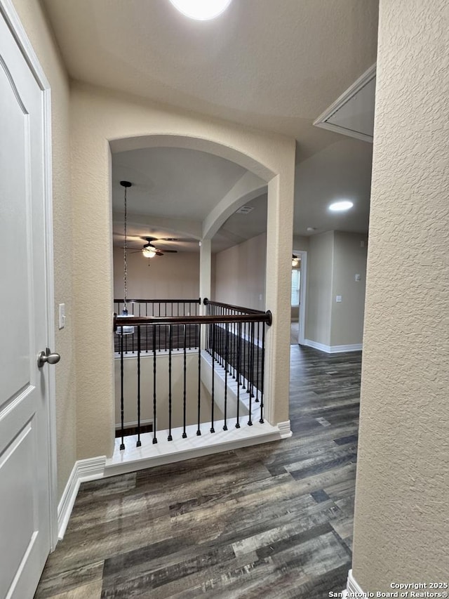 corridor featuring dark wood-style floors, a textured wall, and baseboards