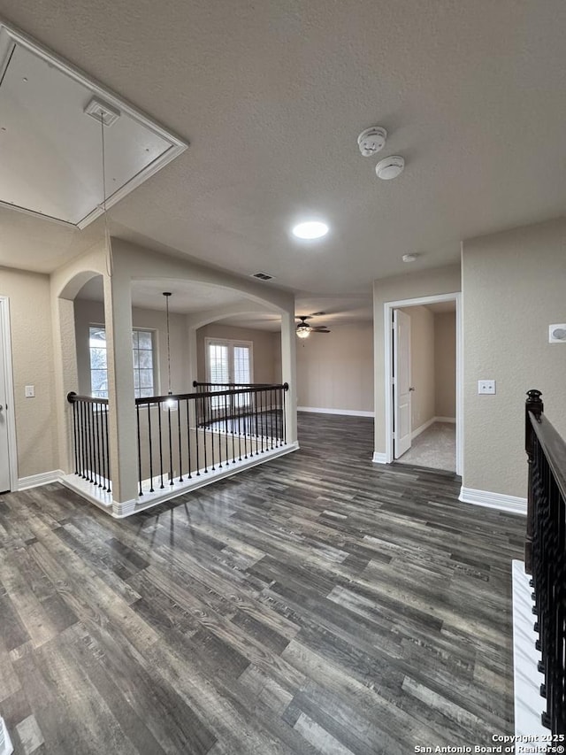 empty room with attic access, a textured ceiling, baseboards, and dark wood-type flooring