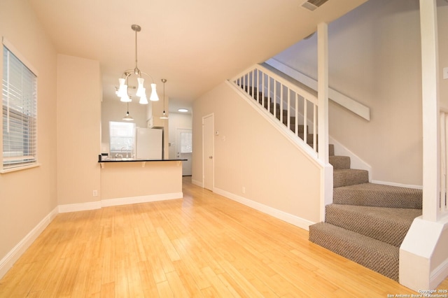 living area featuring stairs, baseboards, light wood-style flooring, and an inviting chandelier