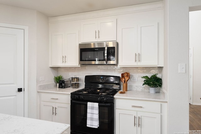 kitchen featuring black gas range oven, stainless steel microwave, and white cabinets