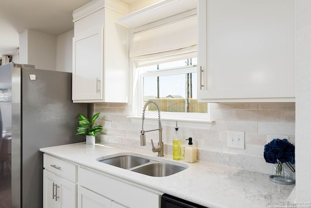 kitchen featuring light stone counters, a sink, white cabinetry, freestanding refrigerator, and tasteful backsplash