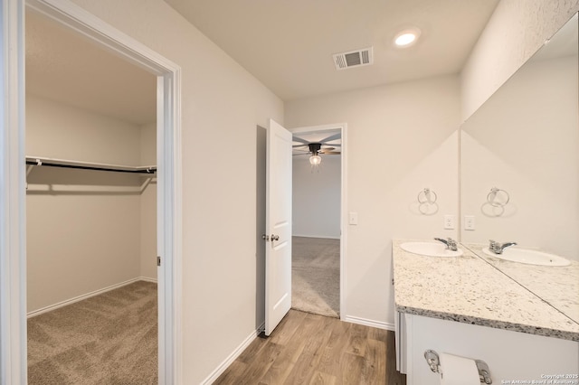 bathroom with wood finished floors, vanity, visible vents, baseboards, and a spacious closet