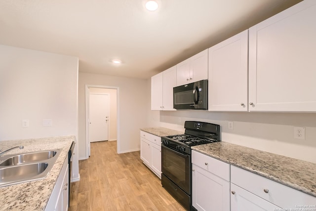 kitchen with light stone counters, light wood-style flooring, a sink, white cabinetry, and black appliances