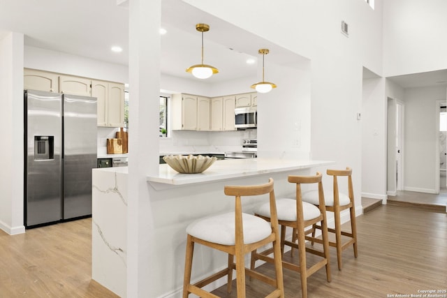 kitchen with a peninsula, visible vents, hanging light fixtures, appliances with stainless steel finishes, and light wood finished floors