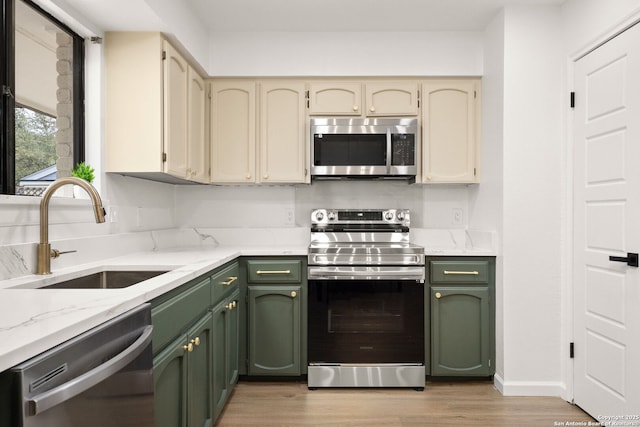 kitchen with cream cabinets, stainless steel appliances, a sink, light wood-style floors, and light stone countertops