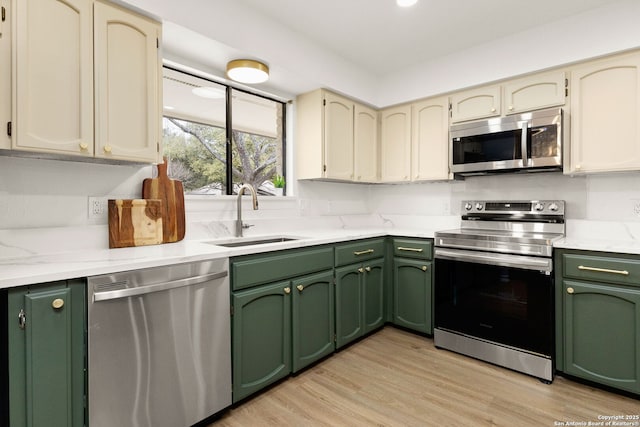 kitchen with light wood-type flooring, green cabinets, stainless steel appliances, and a sink