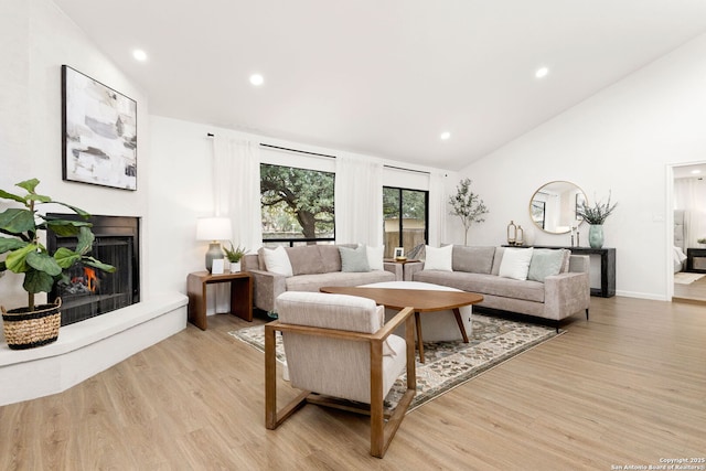 living room with a warm lit fireplace, high vaulted ceiling, light wood finished floors, and recessed lighting