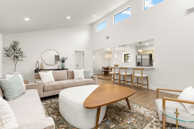 living area with recessed lighting, wood finished floors, a towering ceiling, baseboards, and visible vents