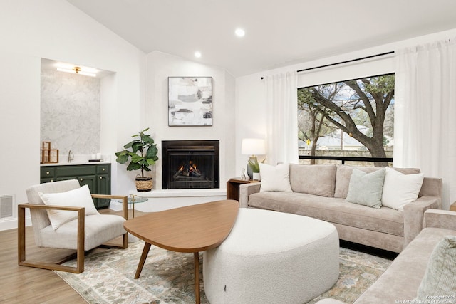 living room with light wood-style flooring, recessed lighting, visible vents, vaulted ceiling, and a lit fireplace