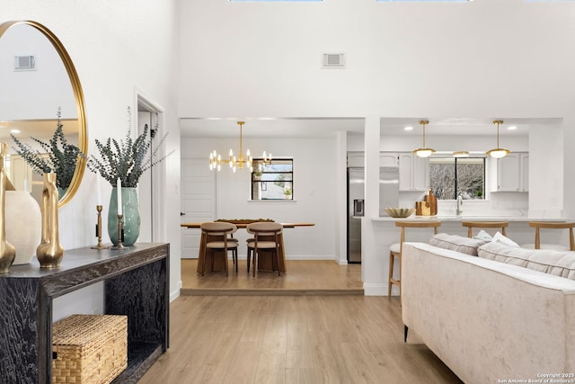 interior space featuring light wood-style floors, visible vents, a towering ceiling, and an inviting chandelier