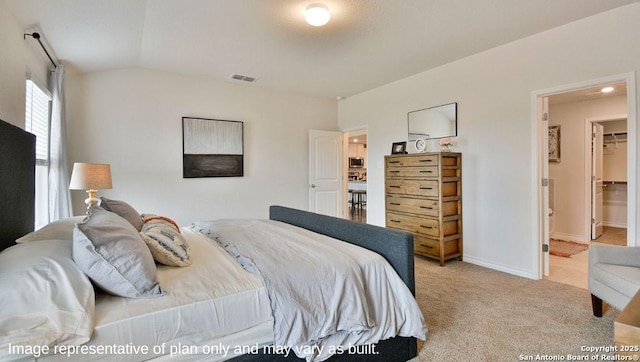 bedroom featuring light carpet, baseboards, visible vents, lofted ceiling, and a walk in closet