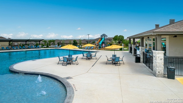 pool featuring playground community, a patio area, a water play area, fence, and an outdoor bar