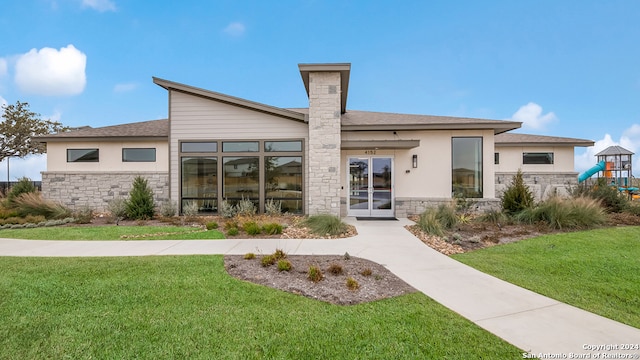 back of property featuring stone siding, a playground, a lawn, and stucco siding