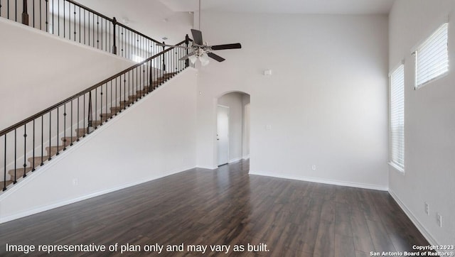 unfurnished living room with arched walkways, dark wood-style flooring, a high ceiling, ceiling fan, and baseboards