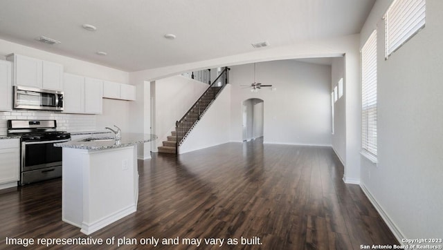 kitchen with stainless steel appliances, open floor plan, a kitchen island with sink, white cabinets, and a sink