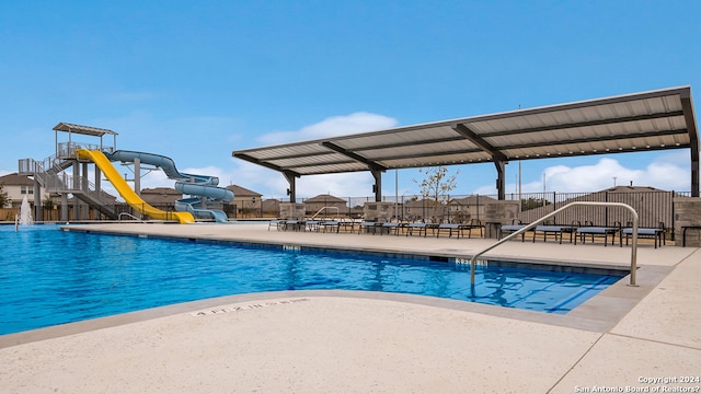 community pool featuring playground community, a water slide, and fence