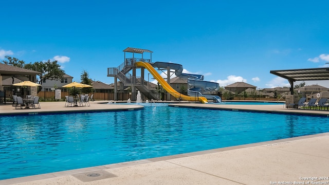 pool with a water slide, playground community, fence, and a patio