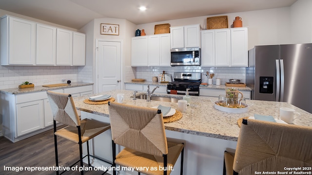 kitchen featuring a center island with sink, appliances with stainless steel finishes, a kitchen breakfast bar, light stone countertops, and white cabinetry