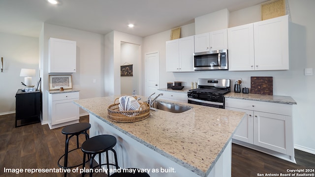 kitchen with stainless steel appliances, light stone counters, a center island with sink, and white cabinets