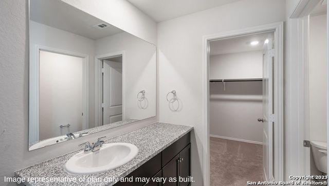 bathroom featuring visible vents, a spacious closet, vanity, and toilet