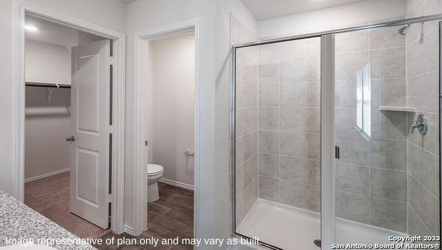 bathroom with wood finished floors, a stall shower, a walk in closet, and toilet