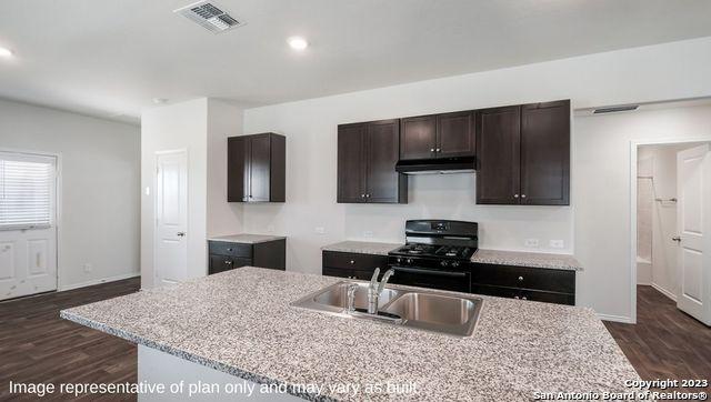 kitchen with black gas range, under cabinet range hood, a sink, visible vents, and a center island with sink