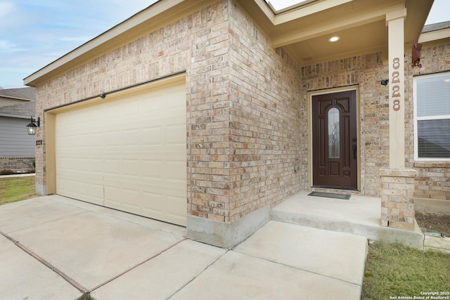 doorway to property with a garage, concrete driveway, and brick siding