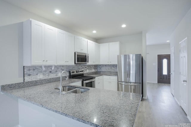 kitchen featuring appliances with stainless steel finishes, white cabinetry, a sink, light stone countertops, and a peninsula