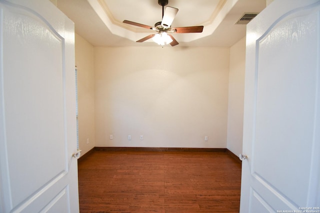 spare room featuring a tray ceiling, wood finished floors, visible vents, and baseboards