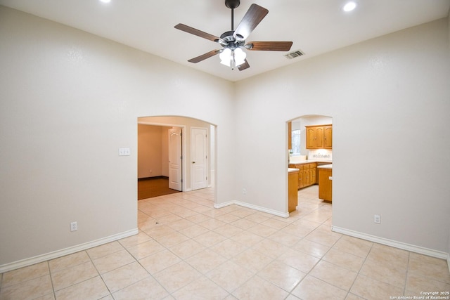 empty room with arched walkways, ceiling fan, light tile patterned flooring, and visible vents