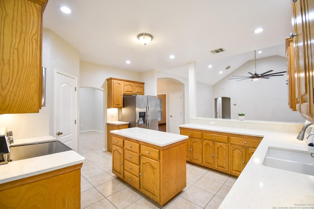 kitchen with a sink, a kitchen island, visible vents, stainless steel refrigerator with ice dispenser, and brown cabinetry