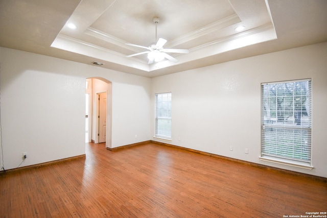 unfurnished room with ornamental molding, a tray ceiling, and arched walkways