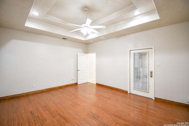 empty room featuring a raised ceiling, crown molding, and wood finished floors